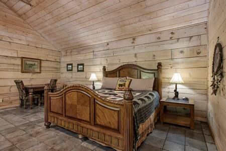Rustic log cabin bedroom with carved wooden bed, nightstands, lamps, and a small desk