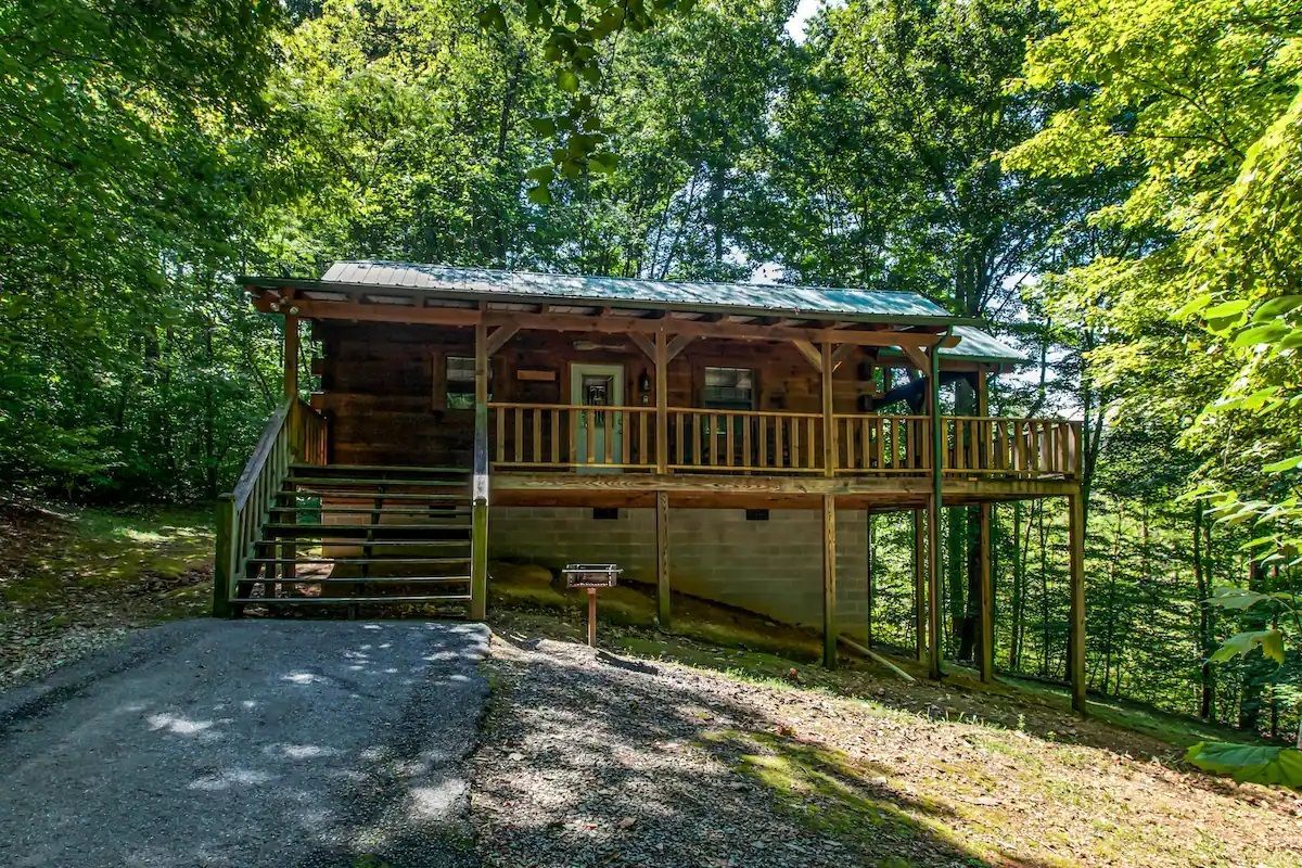 Rustic wooden cabin on a wooded hillside with a porch and gravel driveway