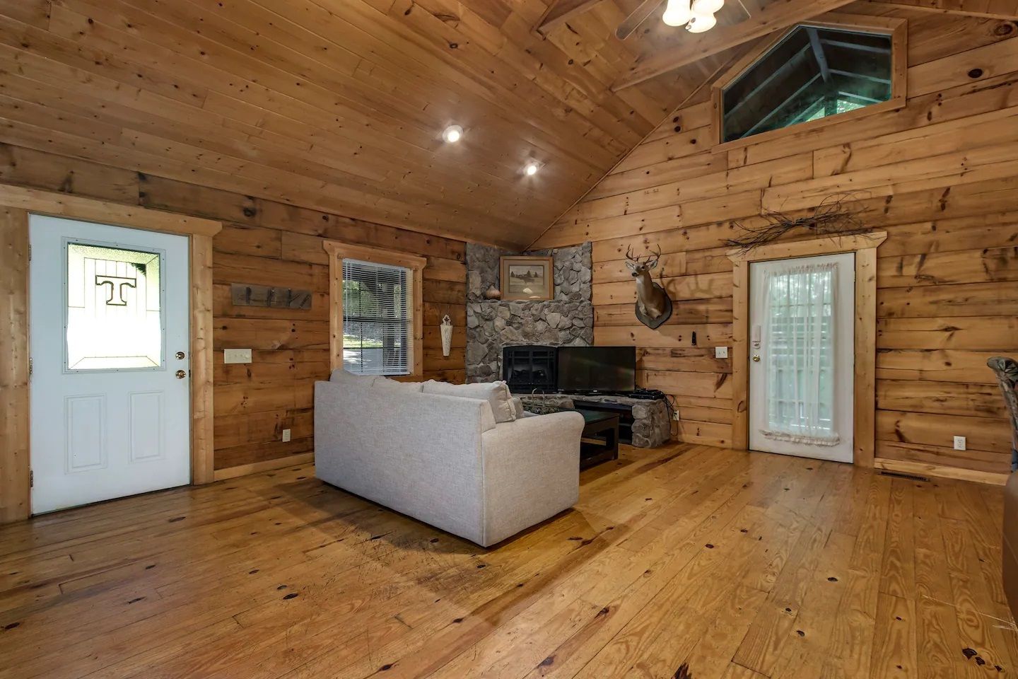 Rustic log cabin living room with wood floors, stone fireplace, and a white sofa under a vaulted ceiling
