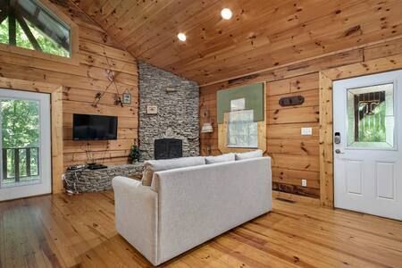 Cozy log cabin living room with stone fireplace, wood walls, white sofa, and large windows