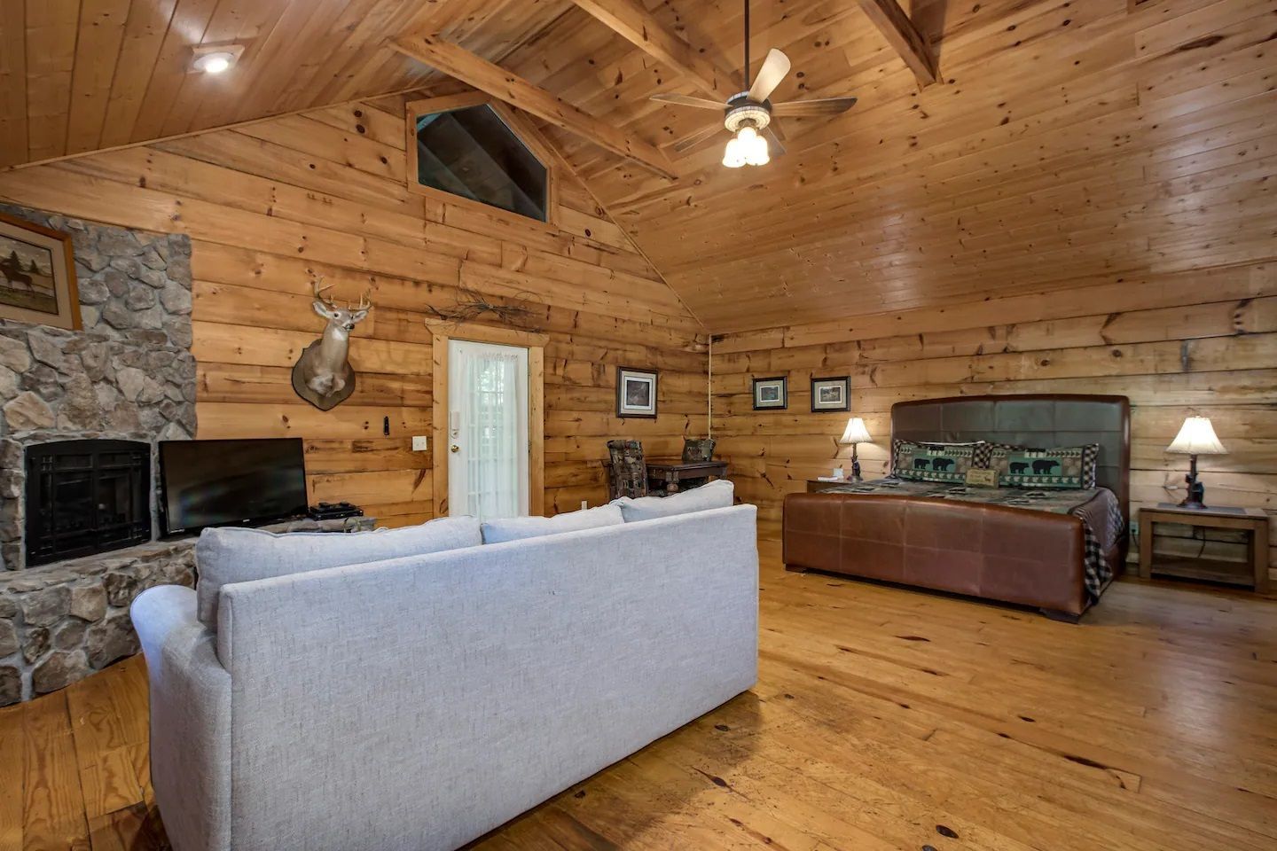 Cozy rustic living room with log walls, stone fireplace, wood ceiling, and leather sofa