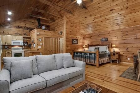 Cozy wood-paneled cabin living room with gray sofa, kitchen area, and dining table