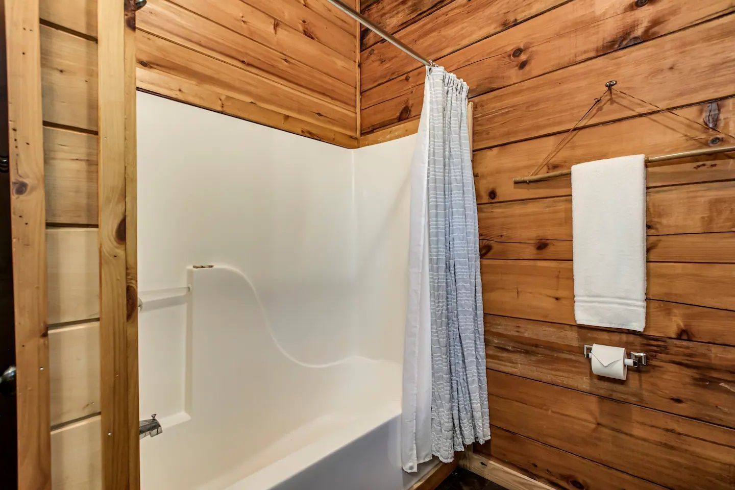 Rustic bathroom with white tub, blue shower curtain, and wood-paneled walls