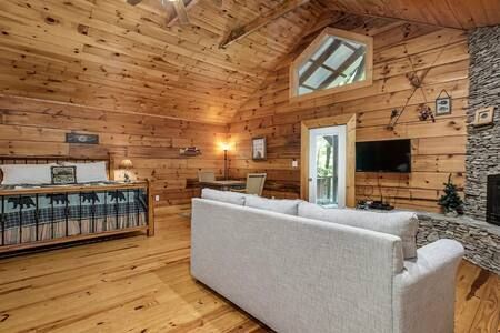 Rustic log cabin living room with gray sofa, wooden walls, fireplace, and wall-mounted TV