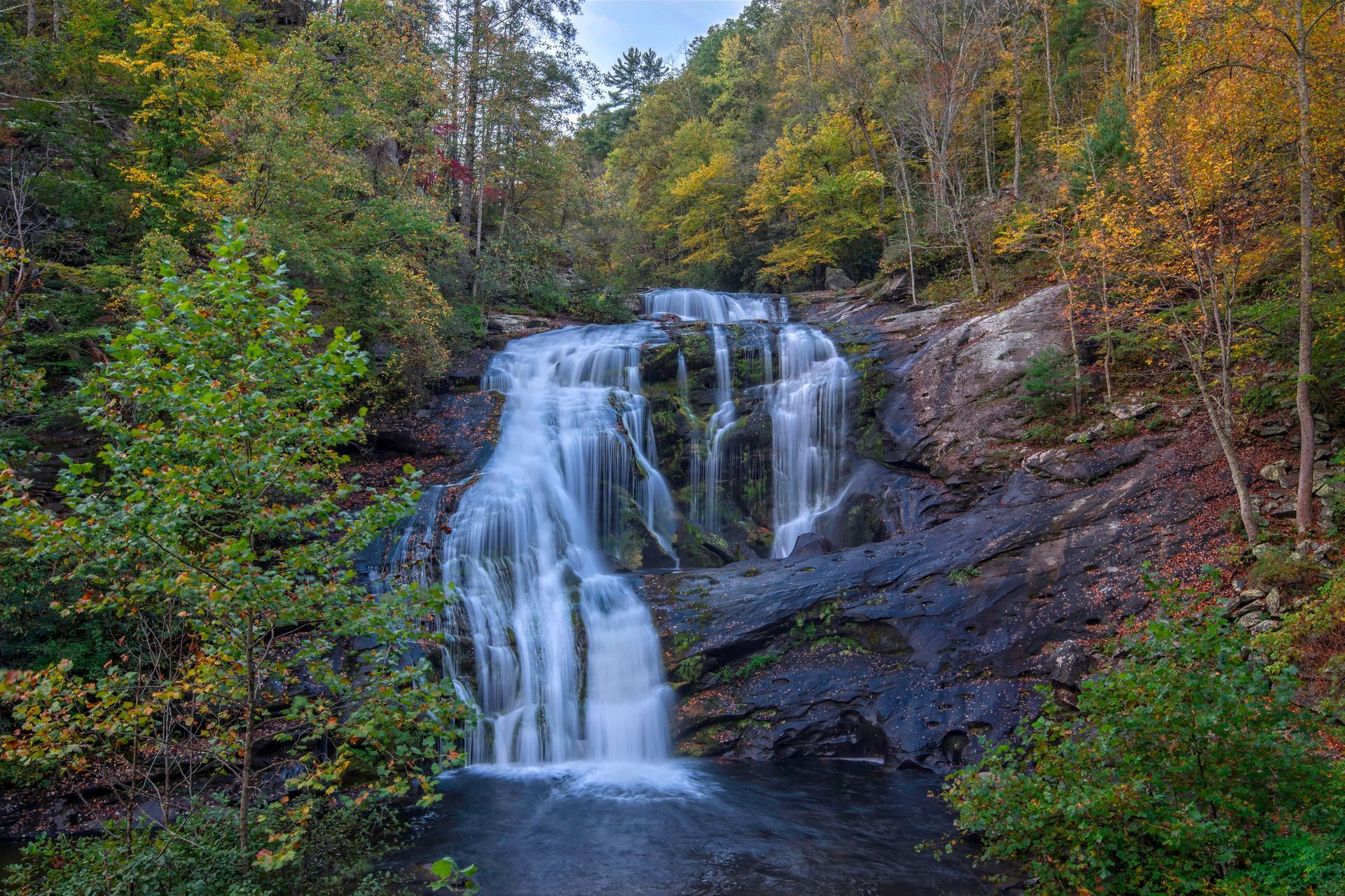 Waterfall cascading over dark rocks in a forest with autumn foliage