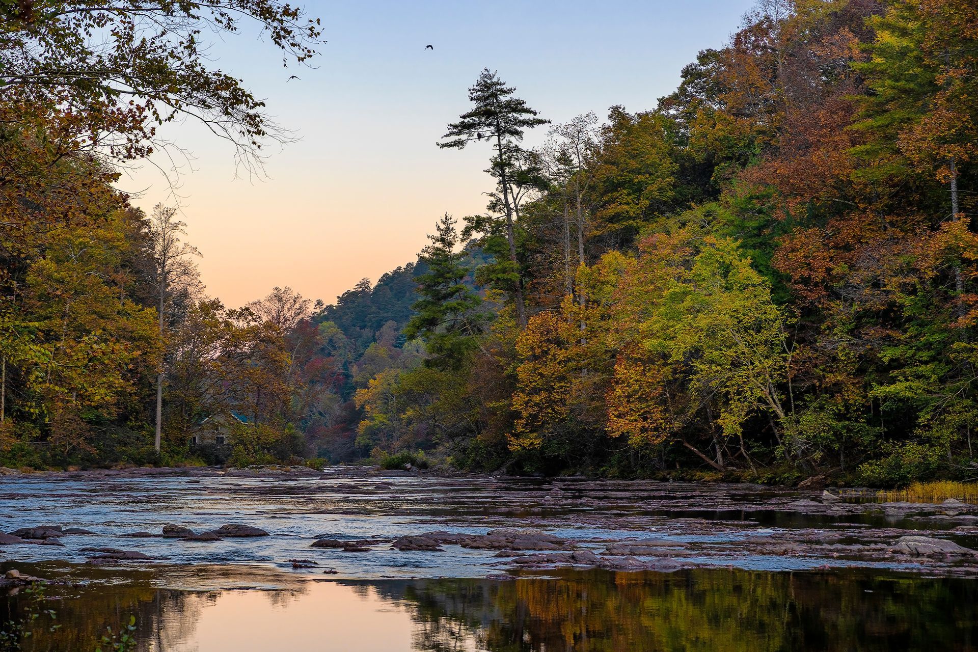 Calm river at sunset reflecting autumn trees and a rocky shoreline in a forested valley