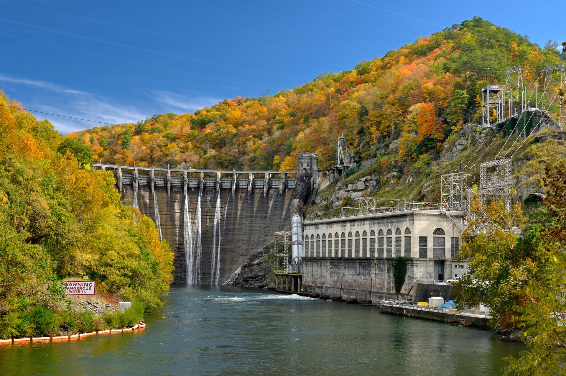 Hydroelectric dam in a river valley with autumn trees and clear blue sky