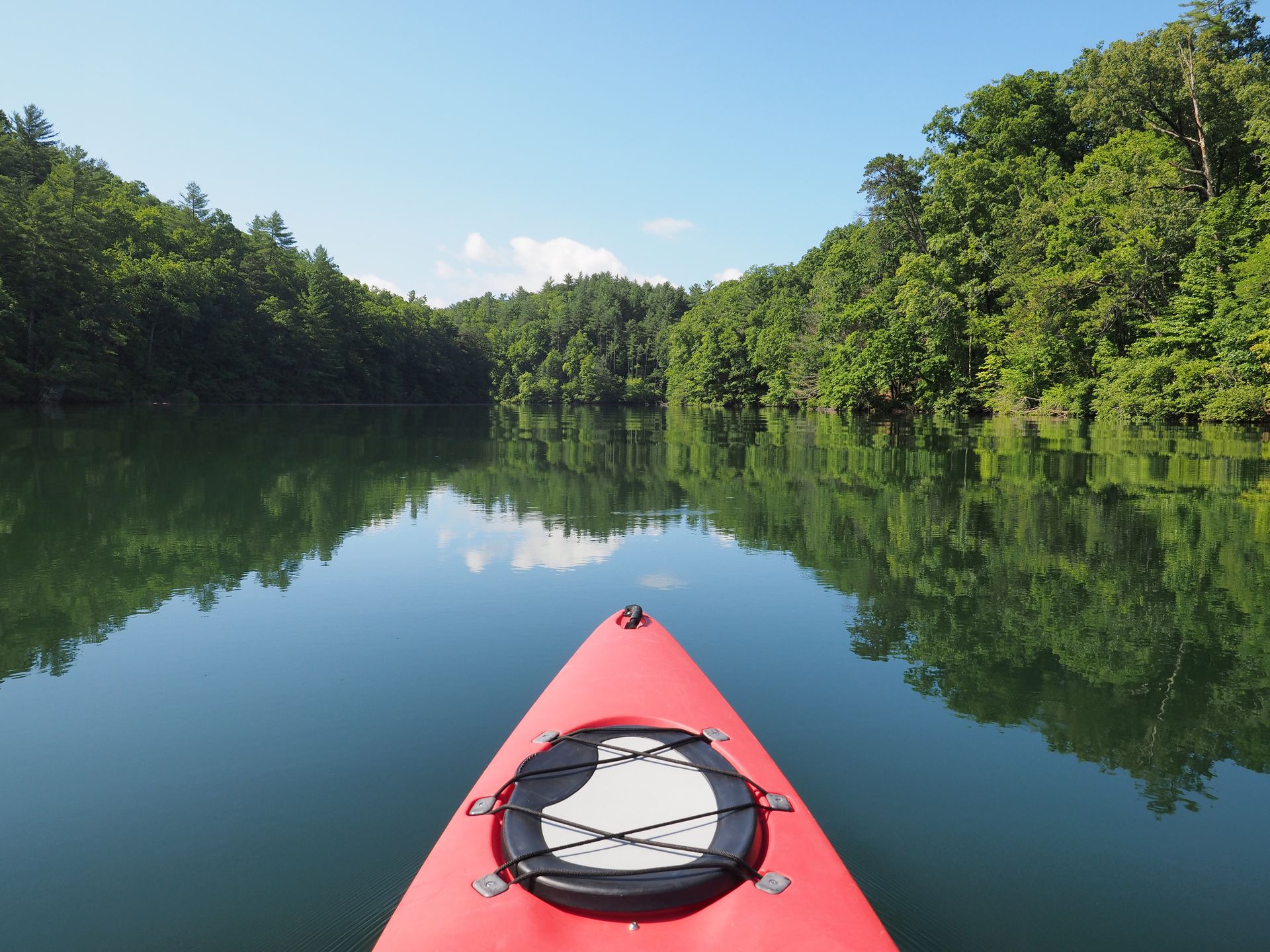Red kayak on calm river reflecting green forest and blue sky
