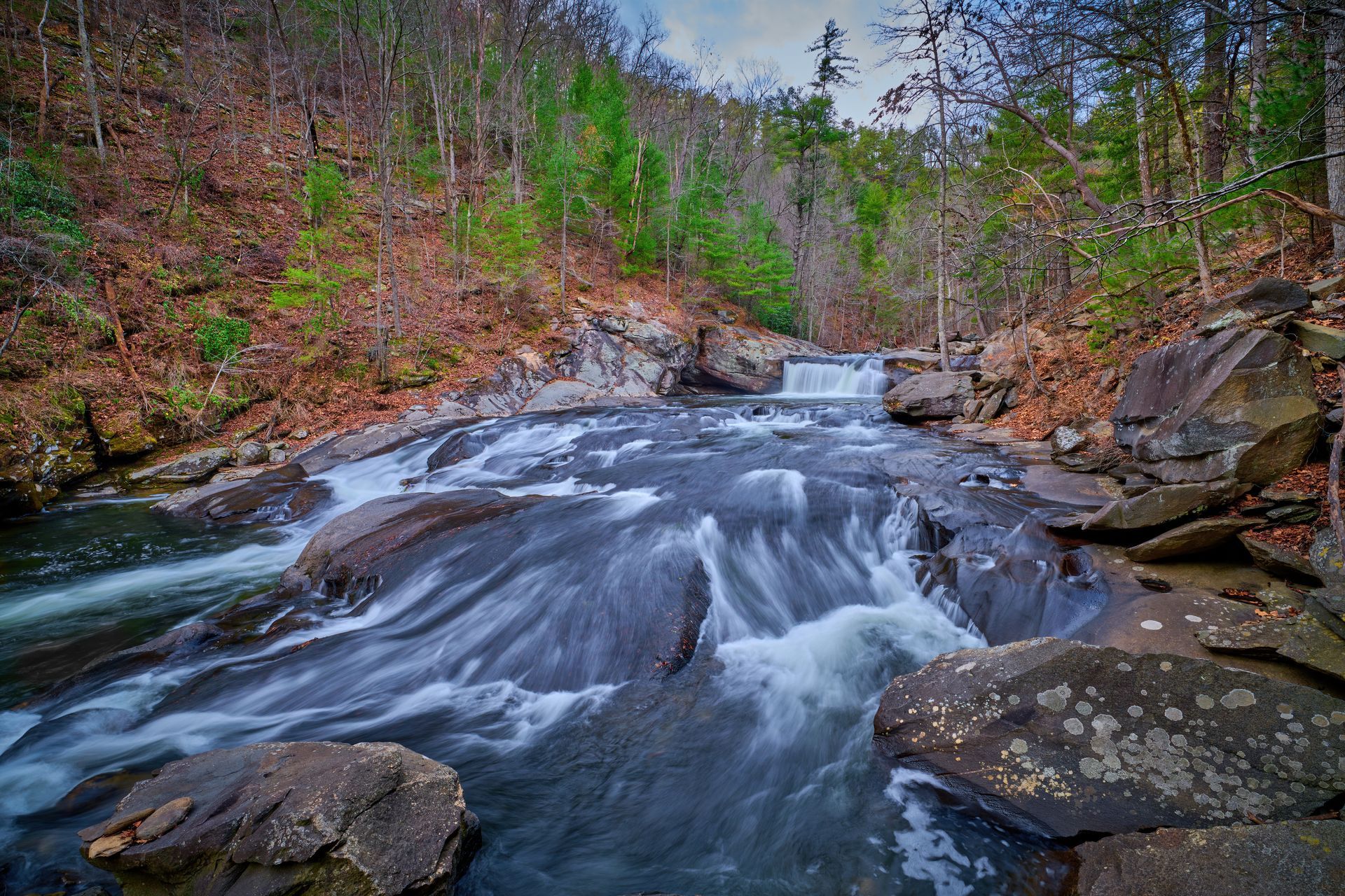Rocky river rapids flowing through a forested canyon in autumn colors