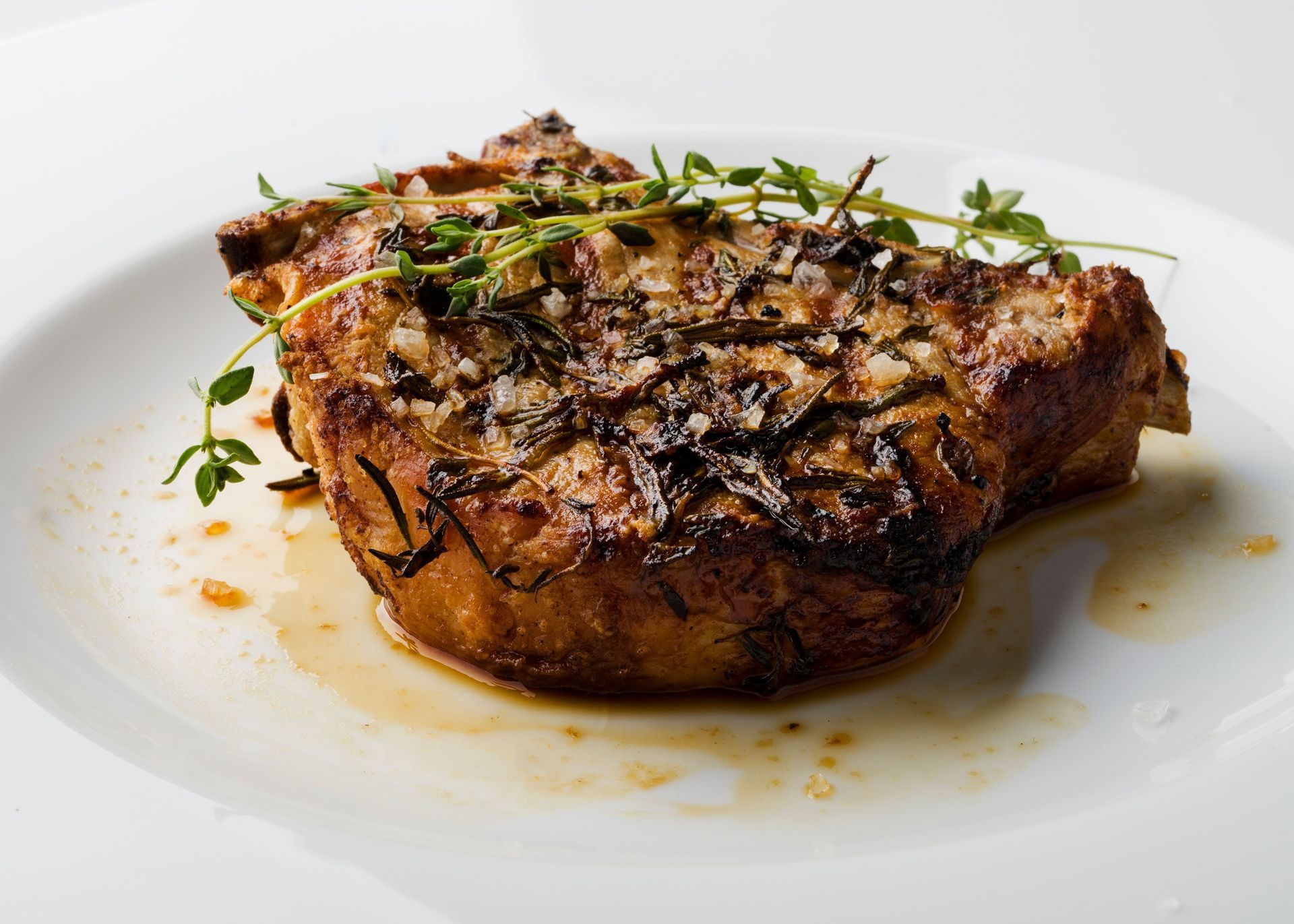 Seared steak topped with herbs, served on a white plate with pan sauce
