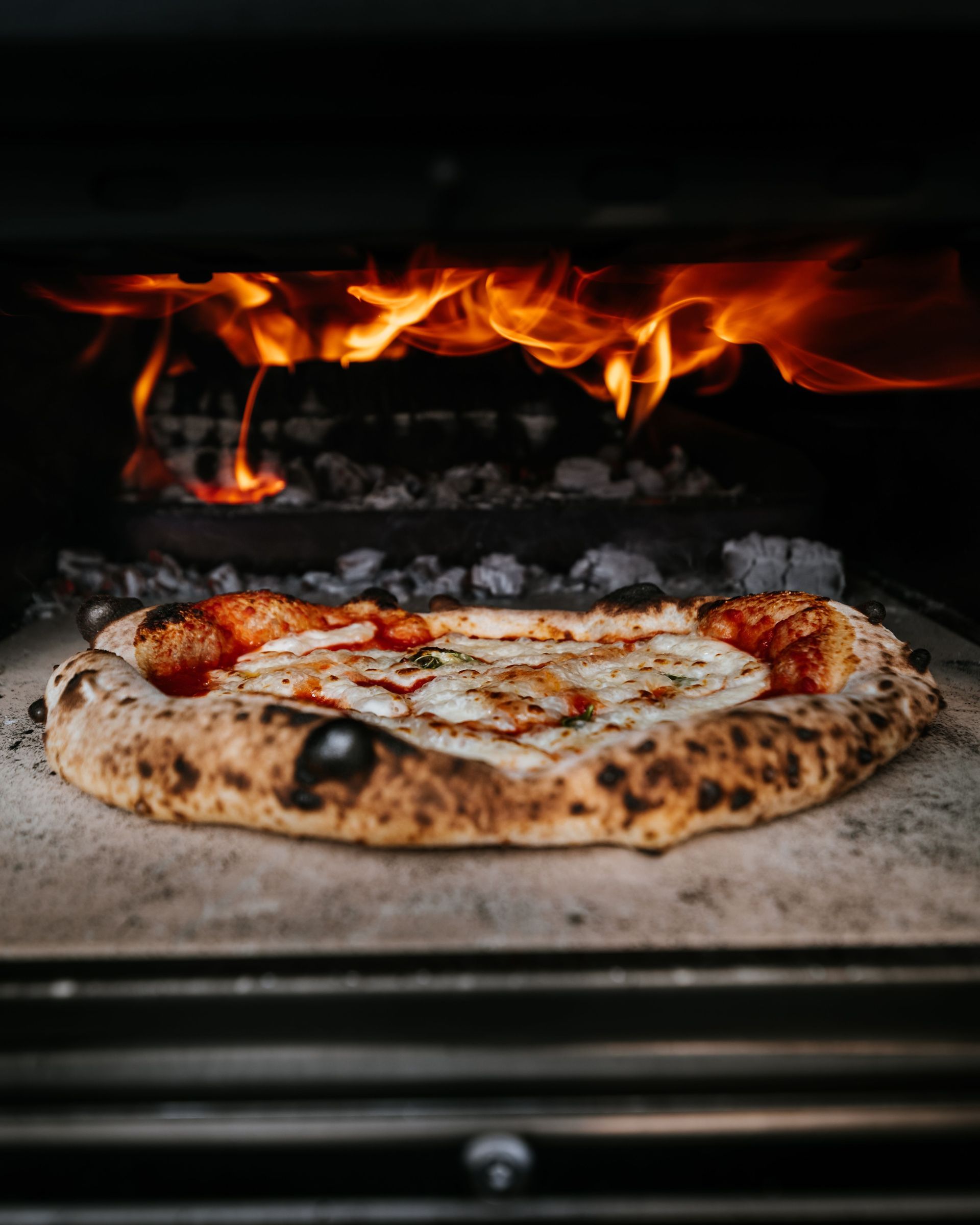 Pizza baking in a wood-fired oven with flames above it