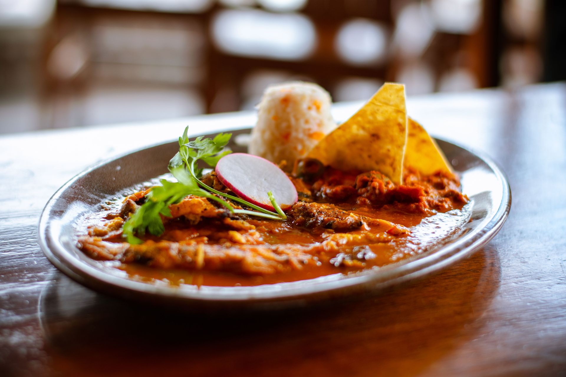 Plate of Indian curry with naan, cilantro, and radish garnish on a wooden table