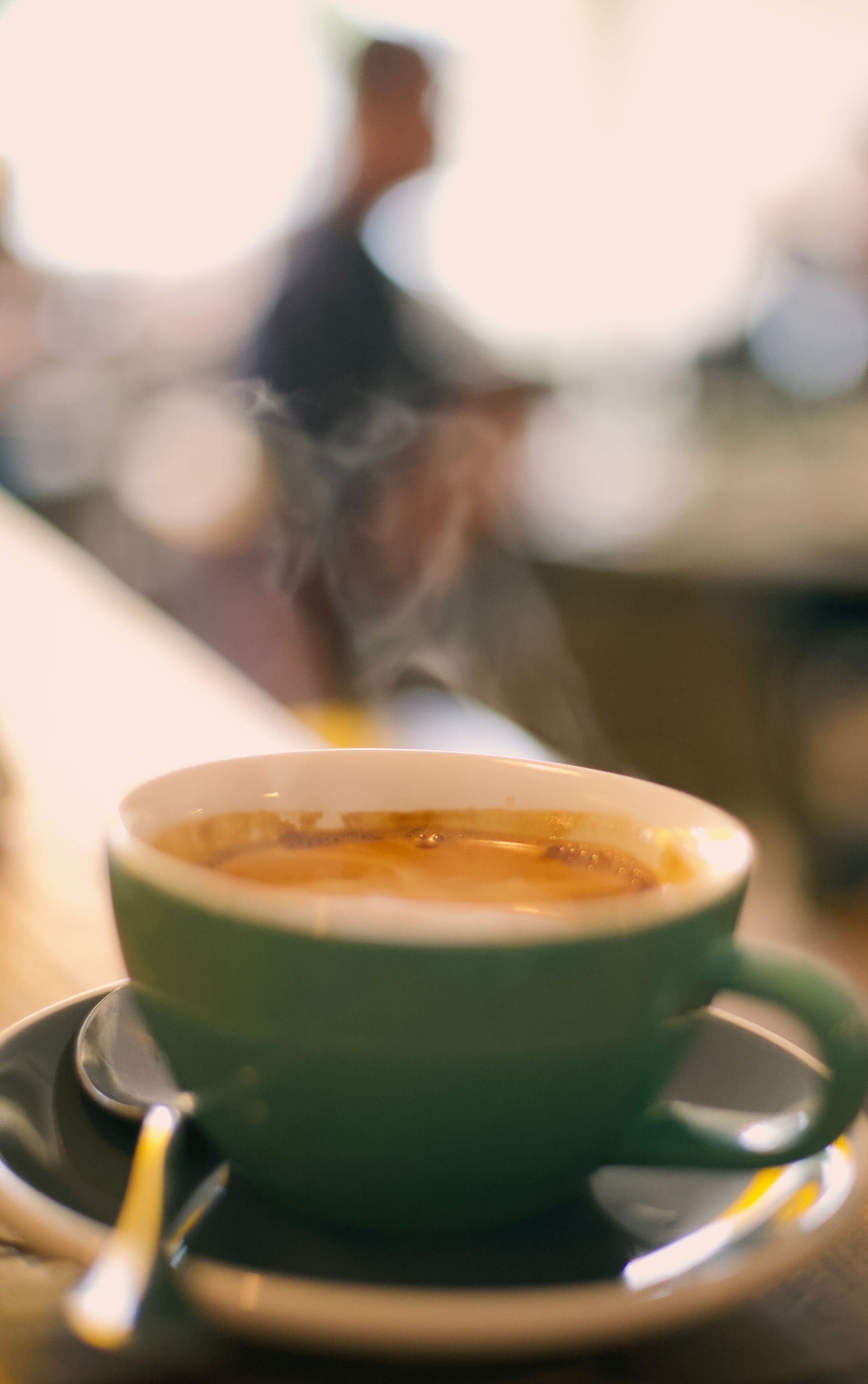 Green coffee cup on a saucer with a spoon, on a table in a softly blurred cafe background
