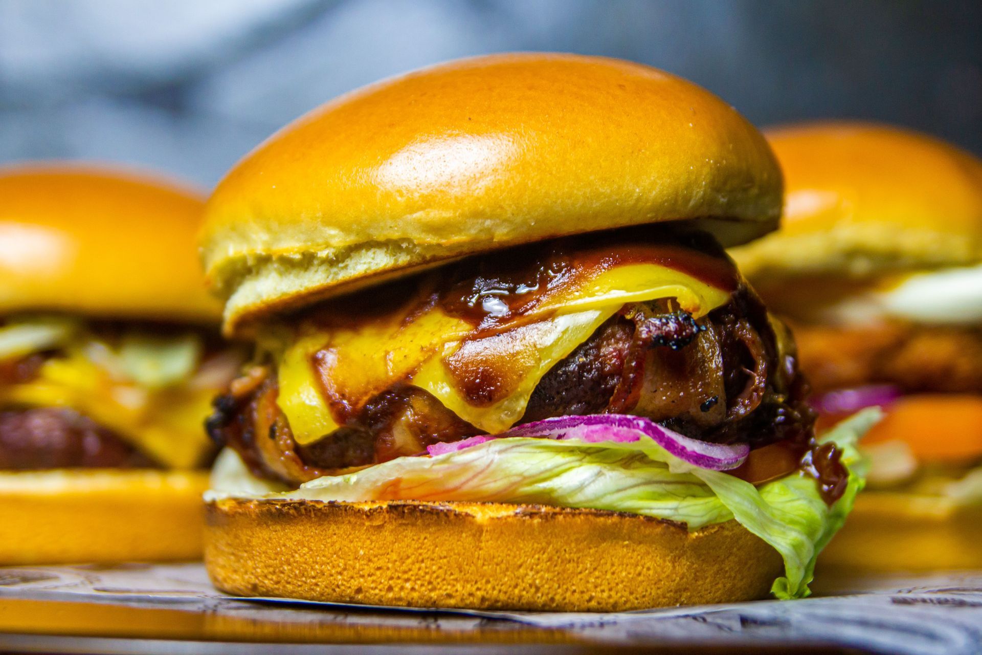 Close-up of glossy cheeseburgers with lettuce and caramelized onions on a tray