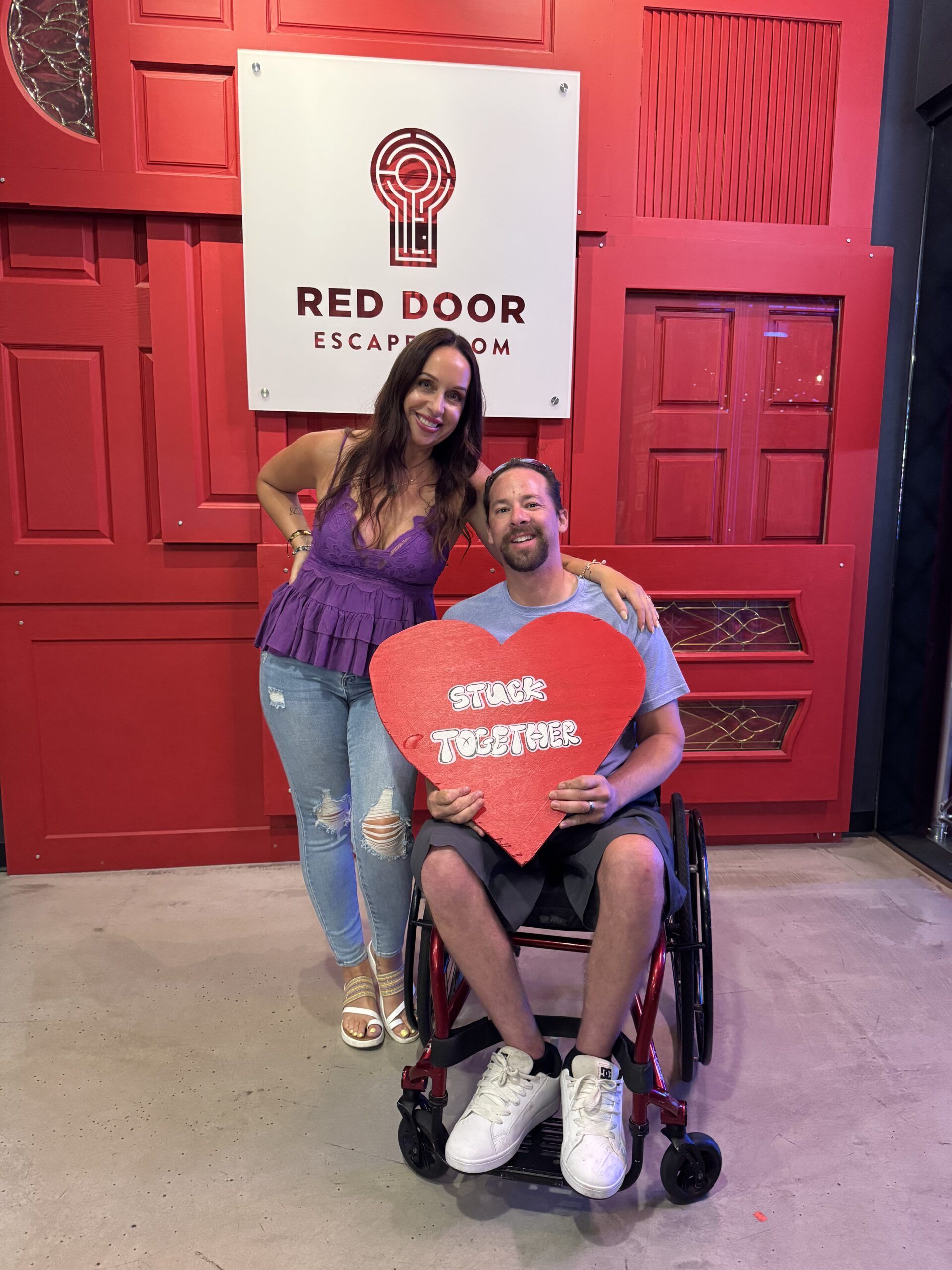 Woman and man in wheelchair pose with a heart prop at 