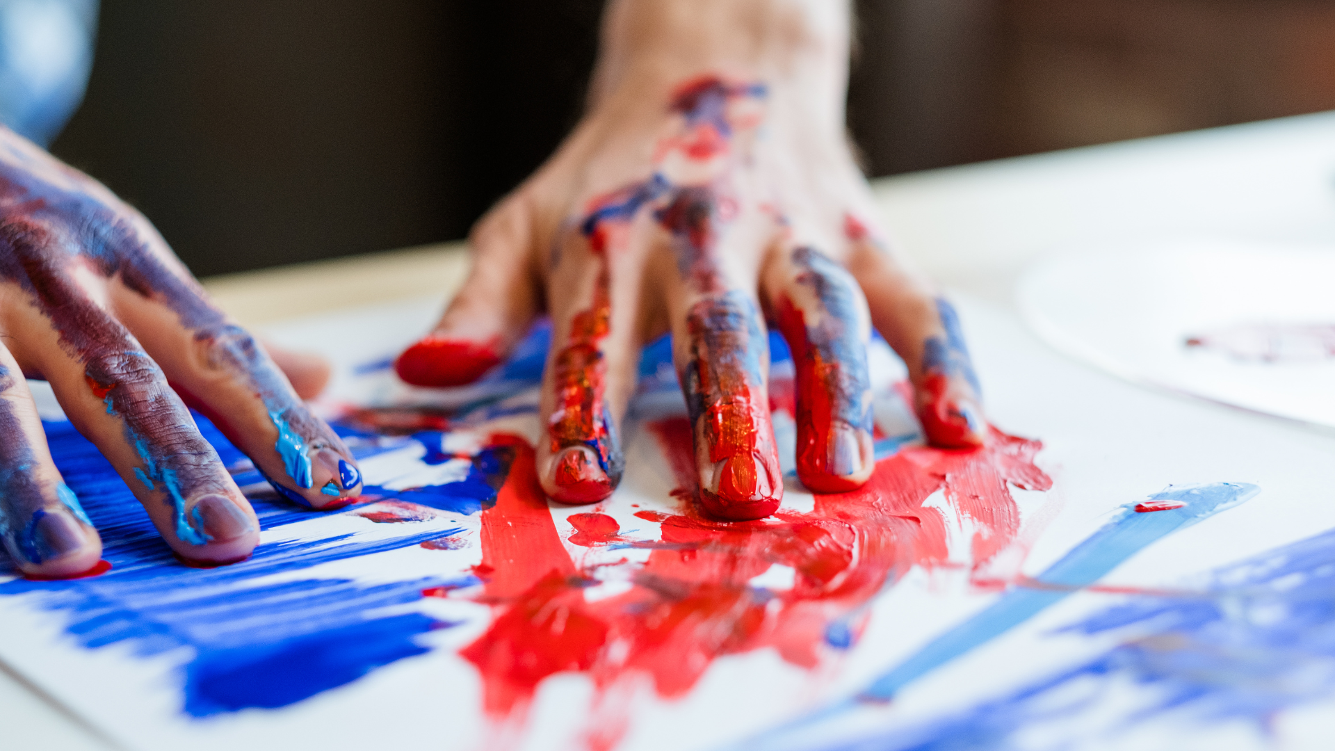 Paint-covered hands press red and blue paint onto white paper during a messy art activity.