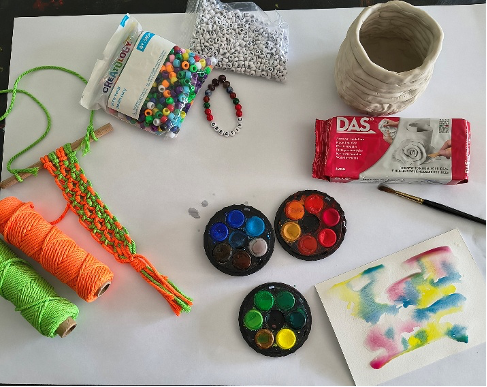 Art supplies on a table: yarn, twine, beads, paints, and a paint-splattered paper.