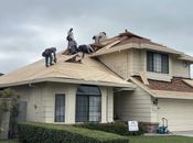 A crew of workers repairs a residential roof with light-colored shingles and exposed wood decking.