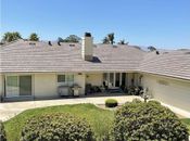A beige, single-story house with a brown tiled roof, a large central chimney, and a concrete patio in the backyard.