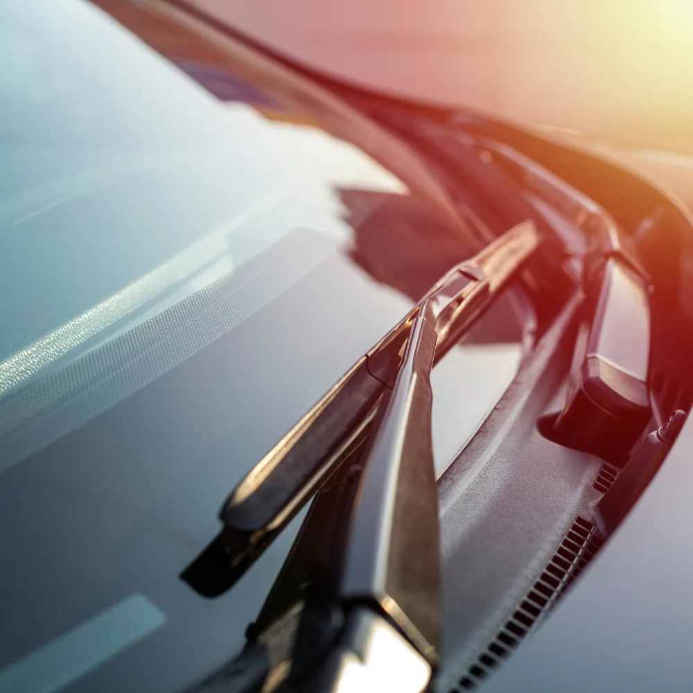 Close-up of car windshield with wiper blades, sunny daytime.