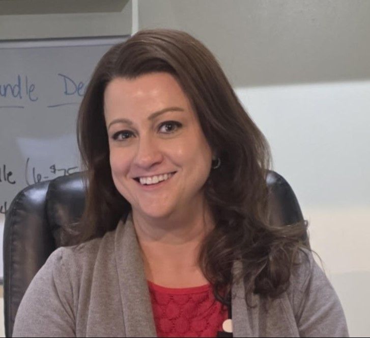 Woman in gray cardigan and red top smiling, looking at the camera; office setting.