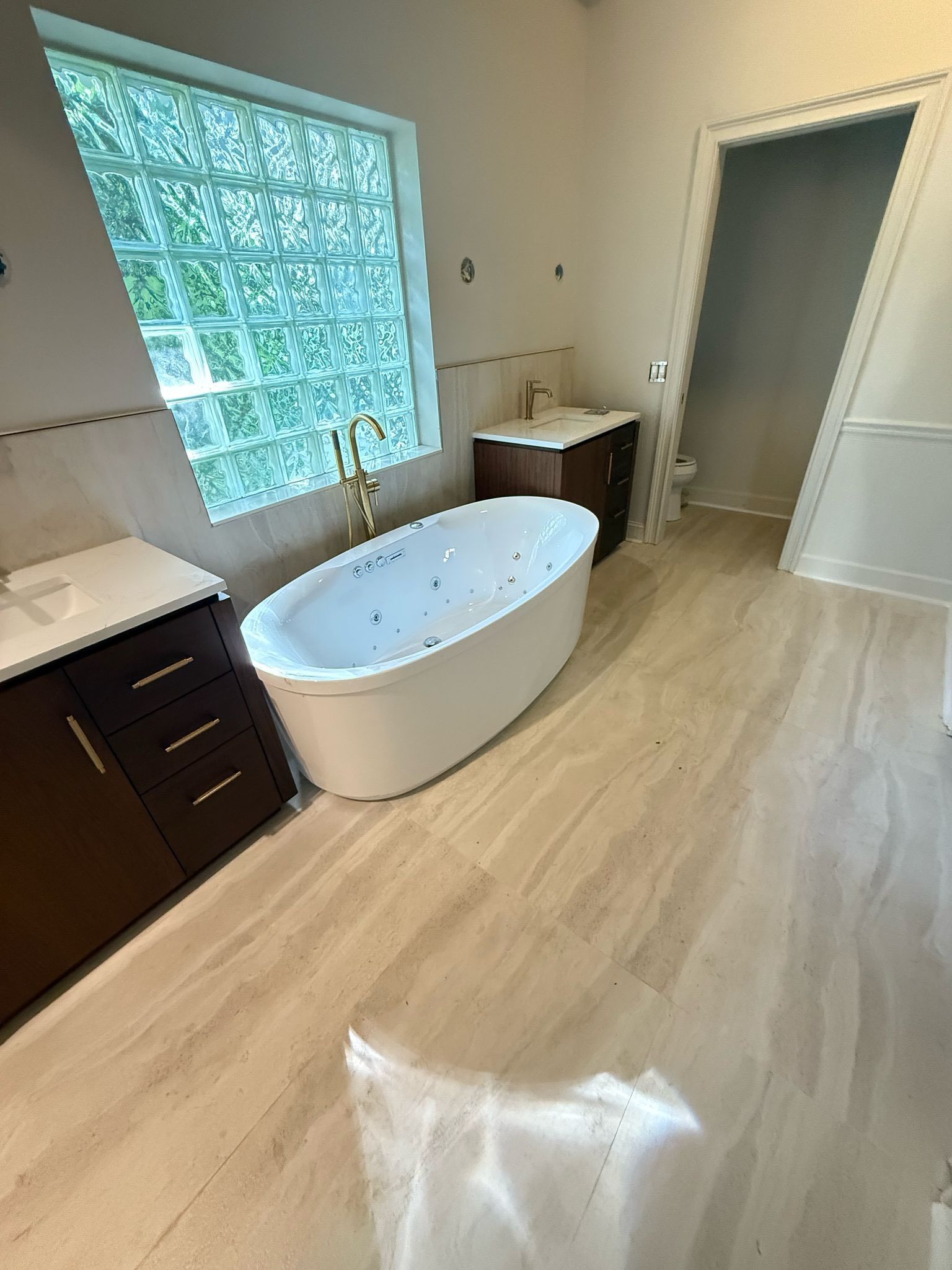 Bright modern bathroom with freestanding tub, vanity, window, and light wood flooring.