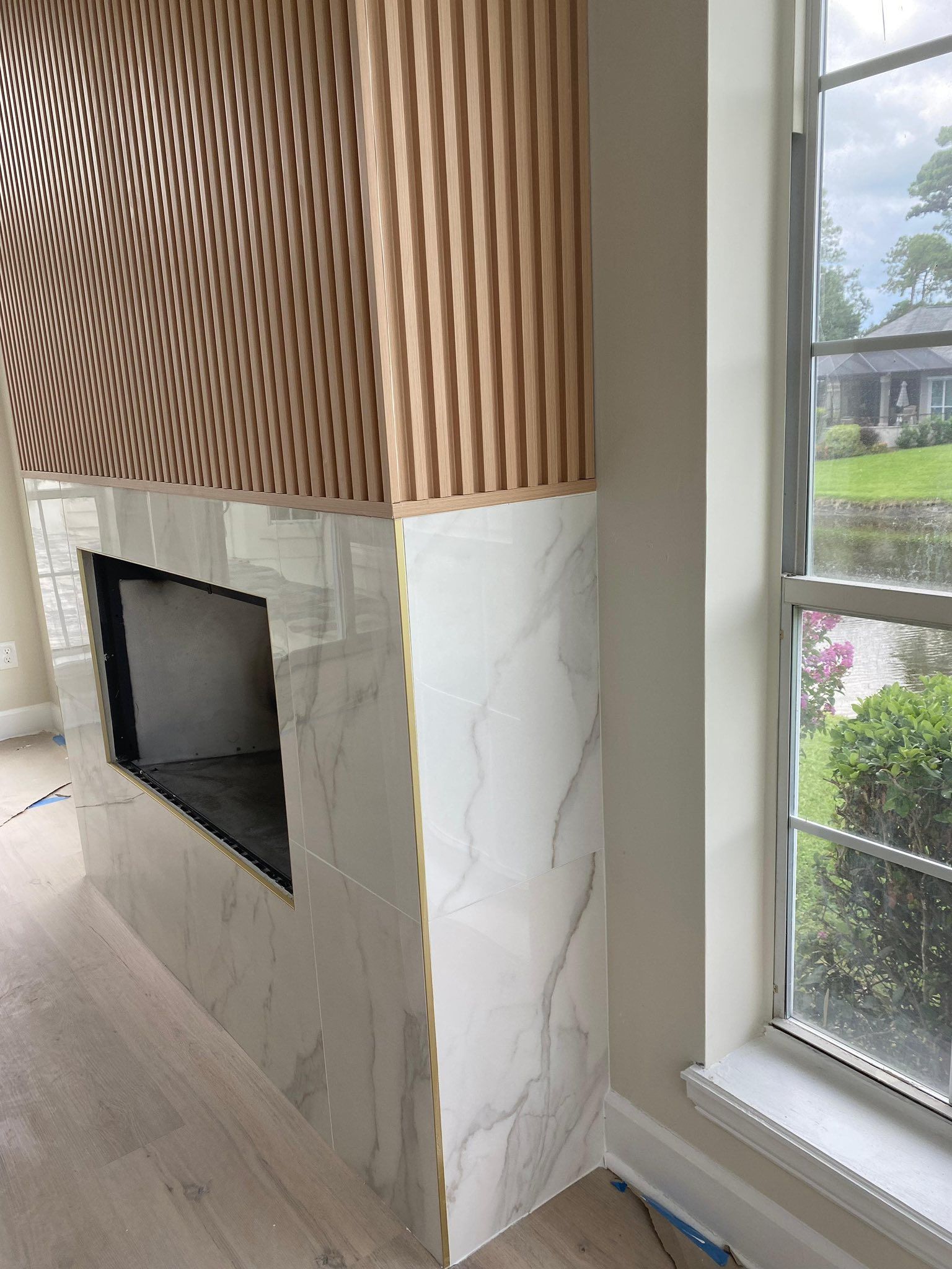 Modern fireplace with wood slat surround, marble base, and window view beside it