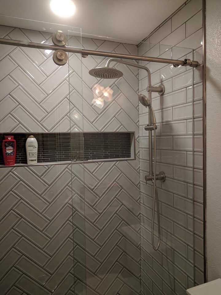 Shower with gray herringbone tile, glass door, and silver fixtures.
