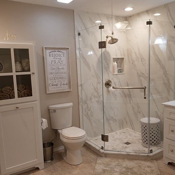Bathroom with white marble tile, glass shower, toilet, and a white storage cabinet.
