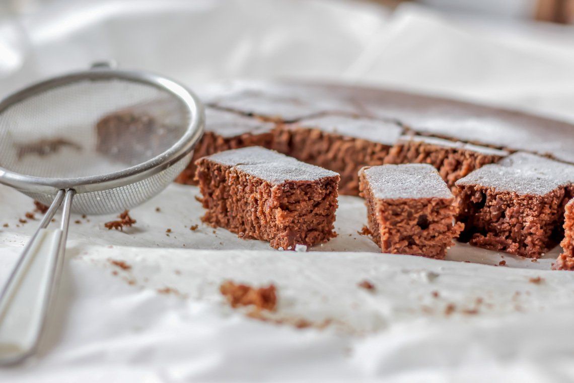 Ein Teller mit Schokoladenbrownies mit Puderzucker und einem Sieb auf einem Tisch.