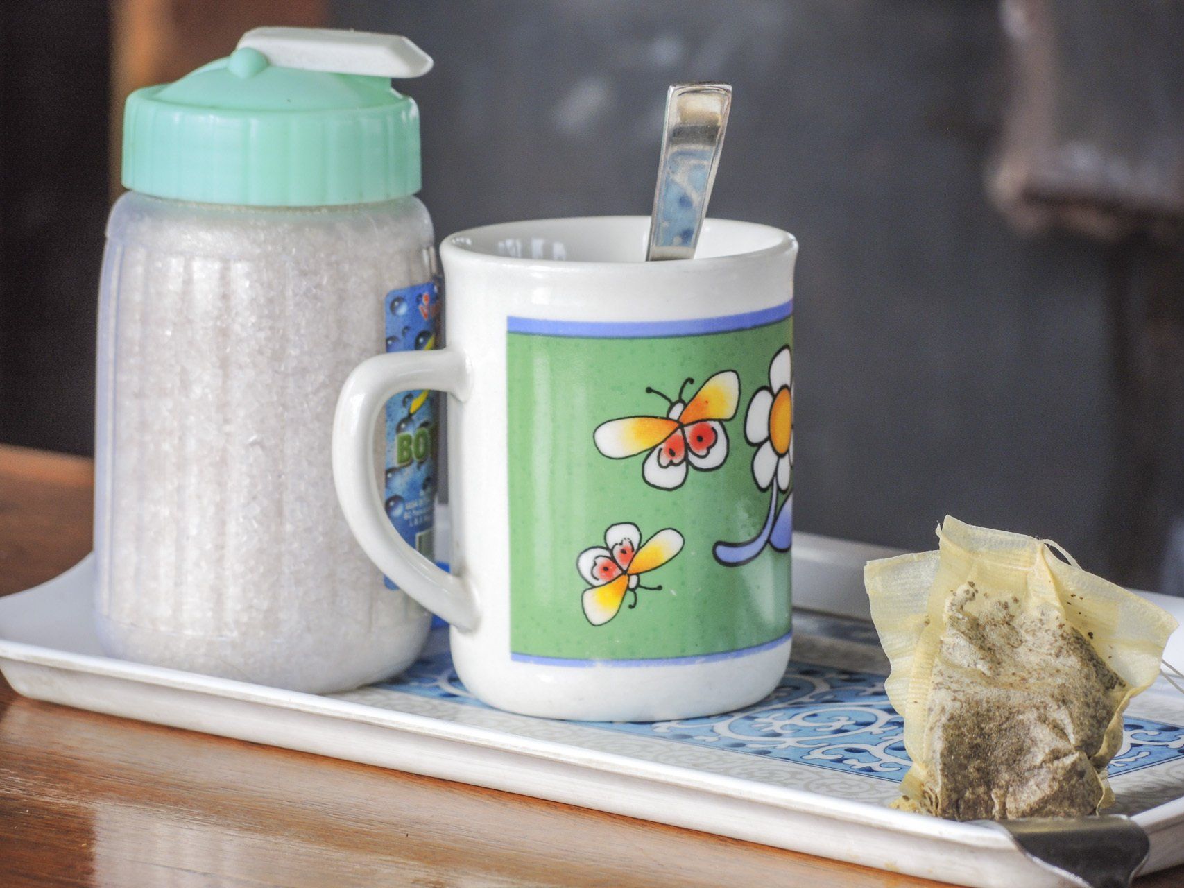 Eine Tasse mit Blumen darauf steht auf einem Tablett neben einem Glas Zucker