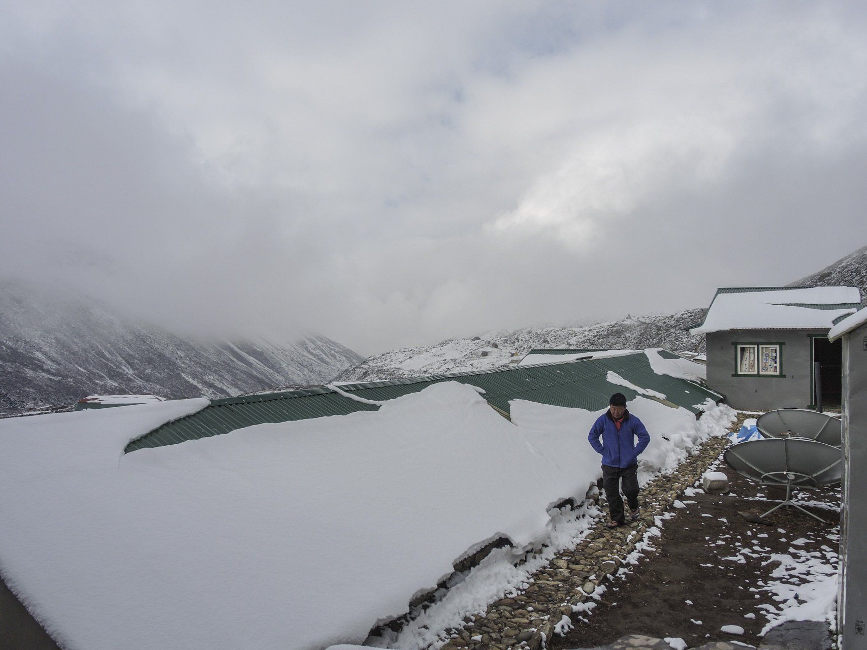 Ein Mann in einer blauen Jacke steht im Schnee in der Nähe eines Gebäudes