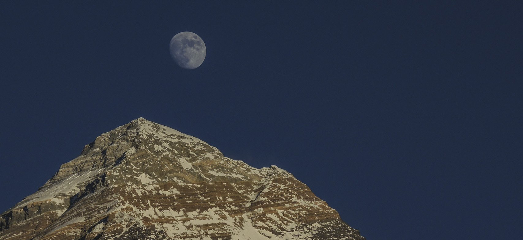 Der Mond geht über einem schneebedeckten Berg auf.
