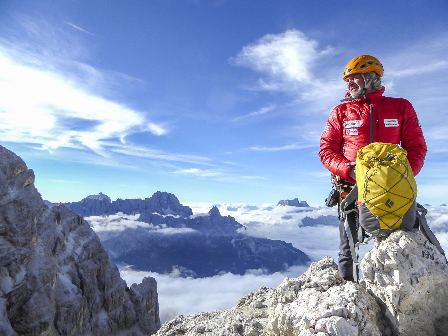 Ein Mann in einer roten Jacke steht auf einem Berggipfel.