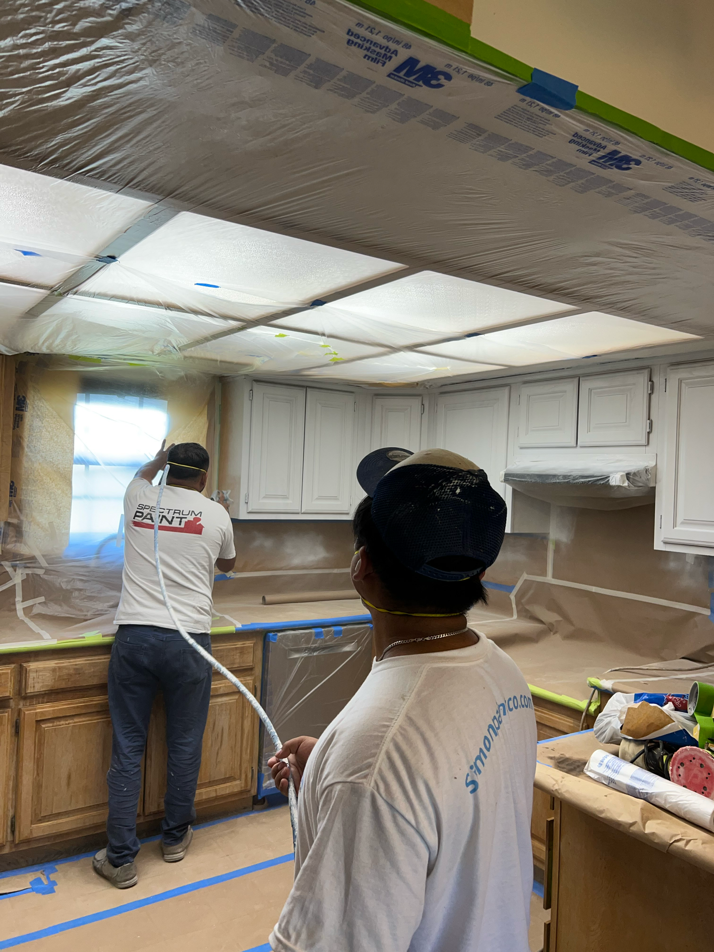 A man is painting a kitchen with a sprayer.