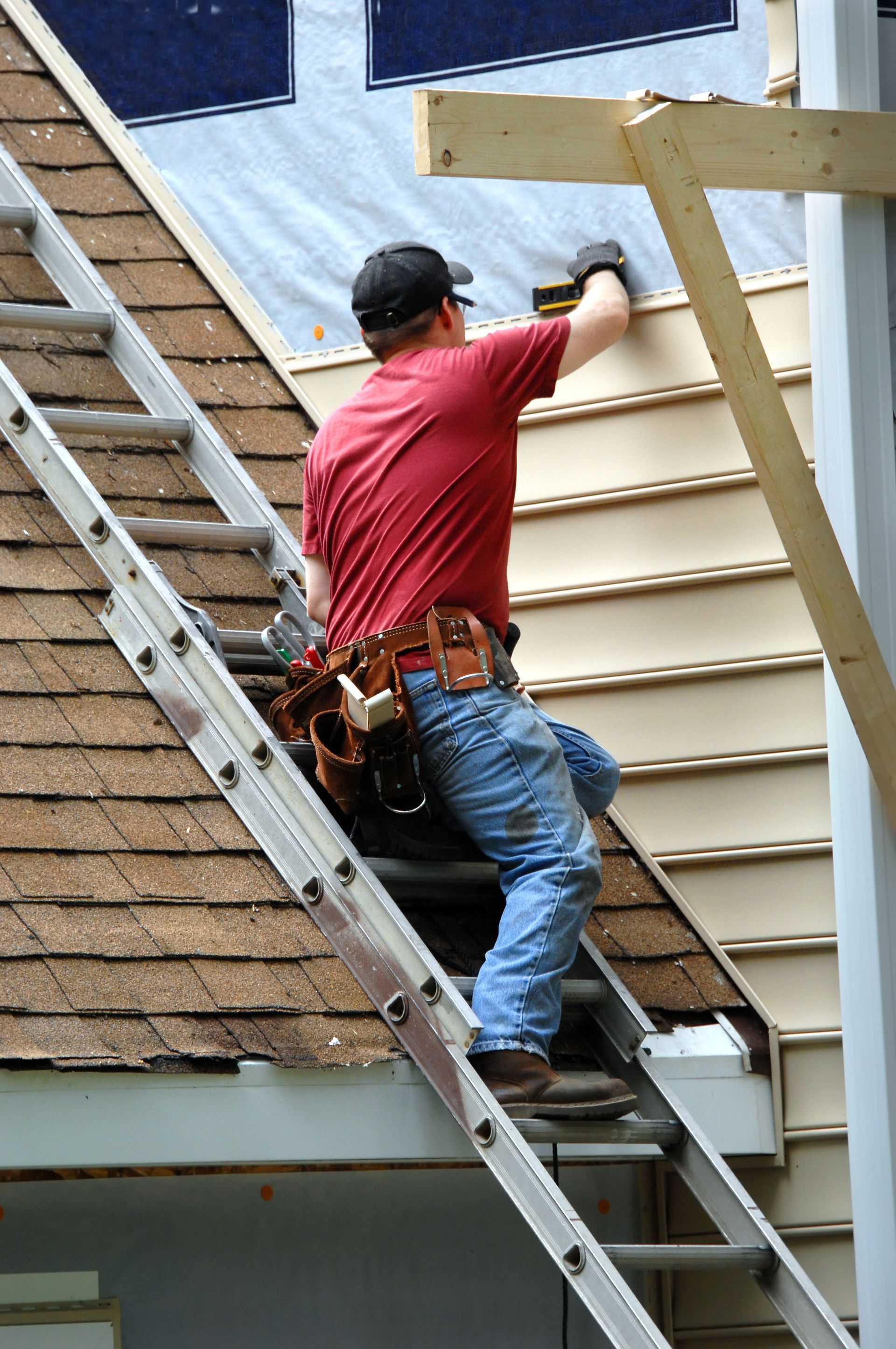 A man is standing on a ladder working on a roof.