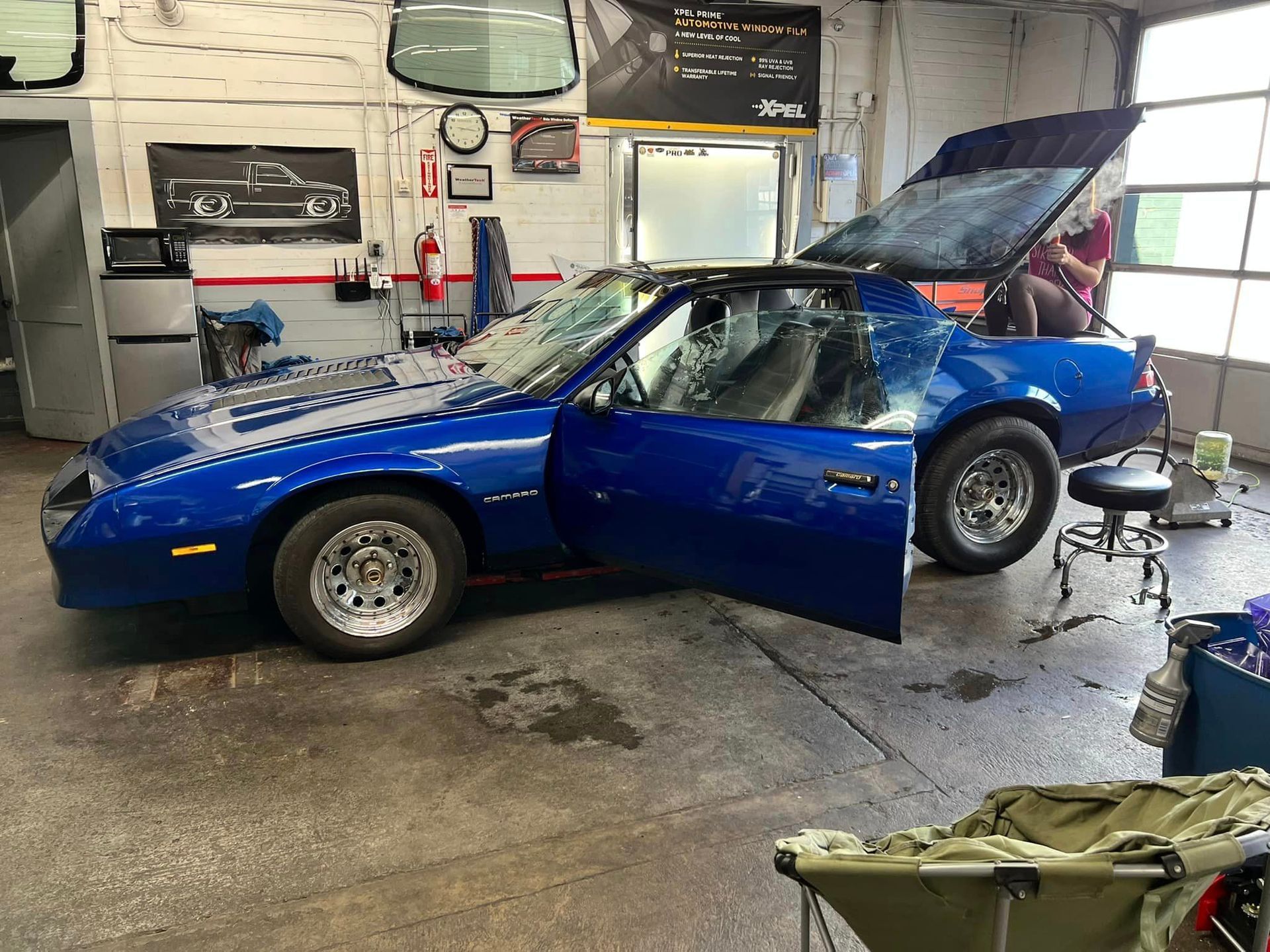 A blue car is parked in a garage with the hood up.