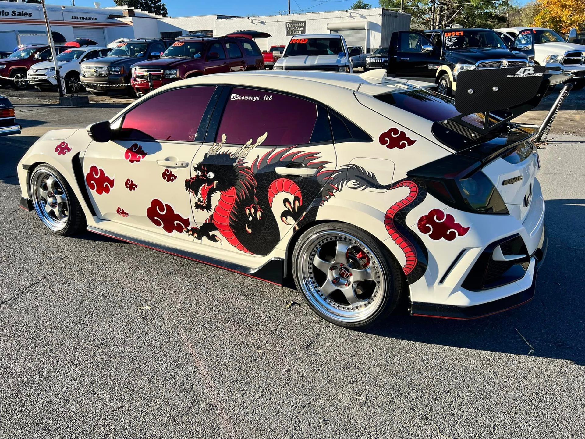 A white car with a dragon on the side is parked in a parking lot.