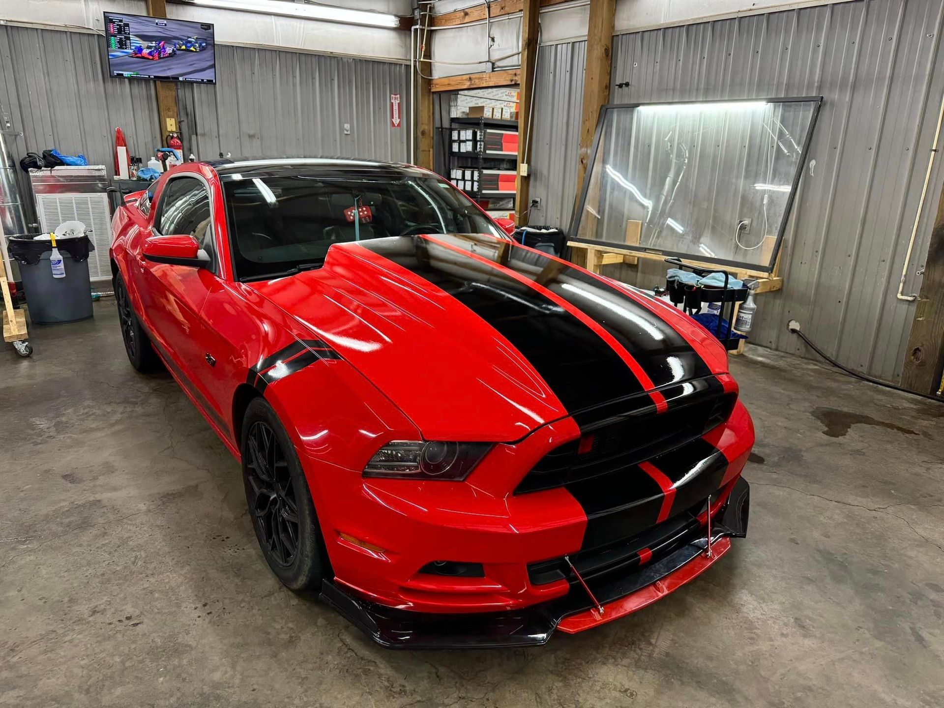 A red mustang with black stripes is parked in a garage.