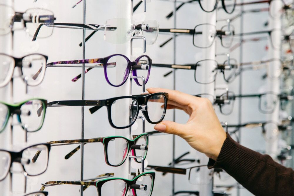 A Person is Holding a Pair of Glasses in Front of a Wall of Glasses — Ian Emslie Optometrist In Warners Bay, NSW