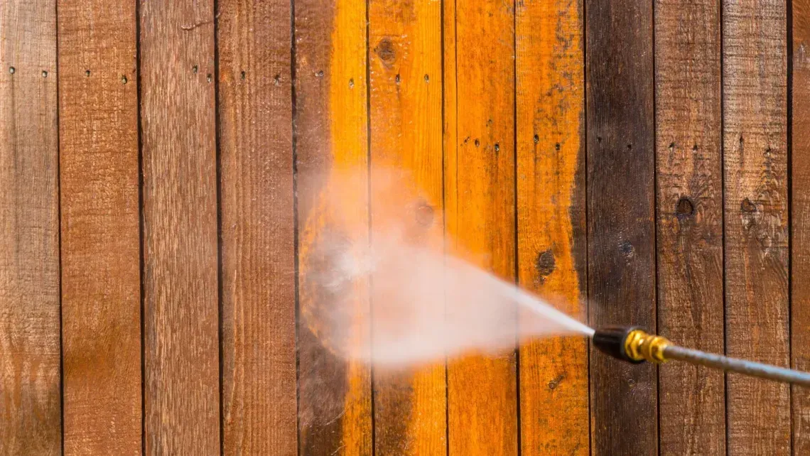 Pressure washer spraying a wooden fence, cleaning a section of orange-stained boards
