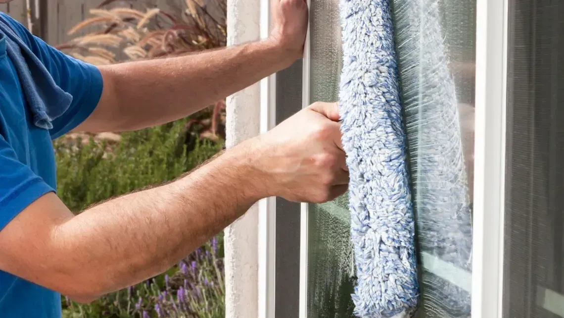 Hands washing a window with a blue microfiber cloth outdoors
