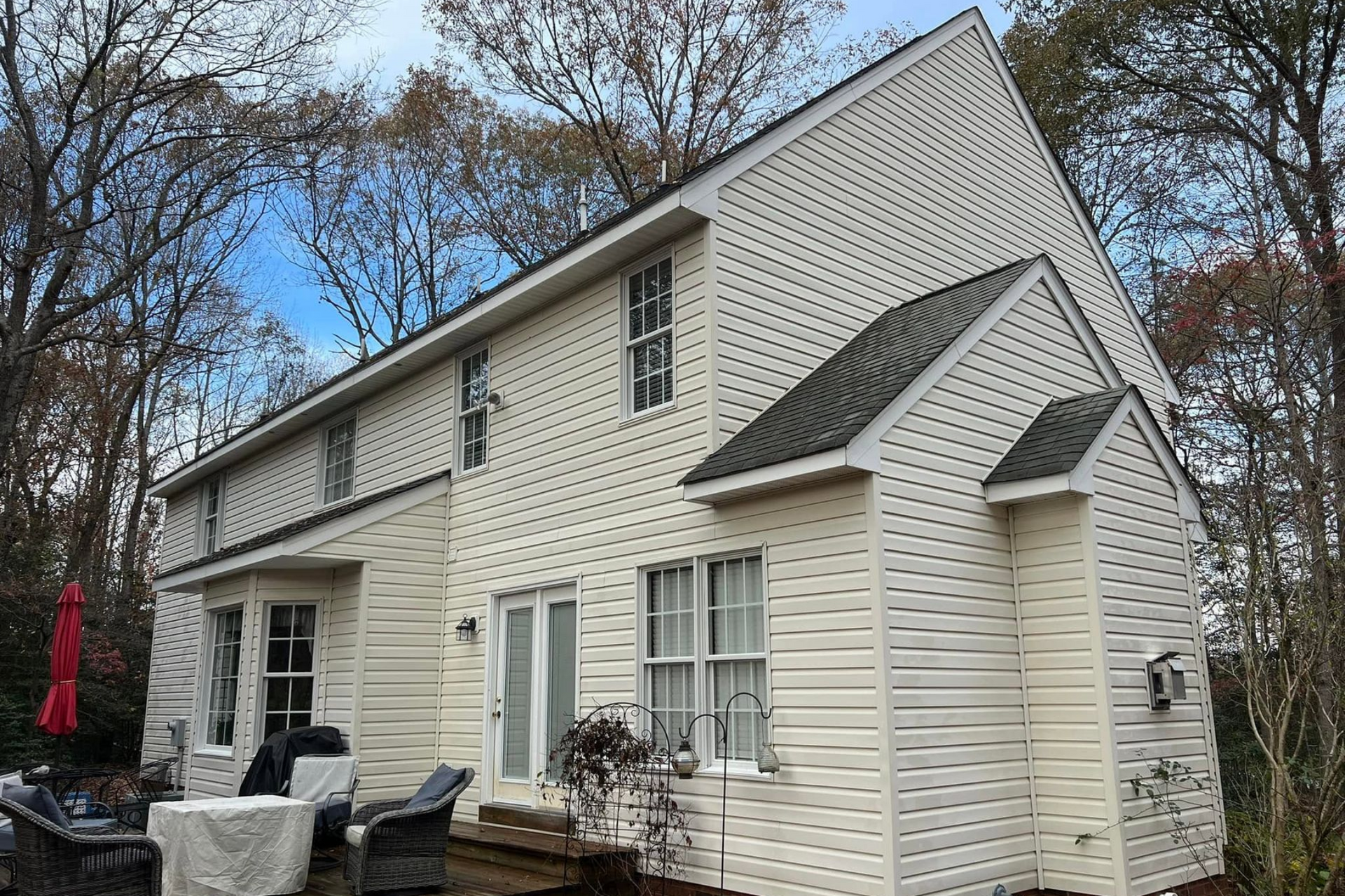White two-story house with black roof, white siding, patio furniture, and autumn trees outside.