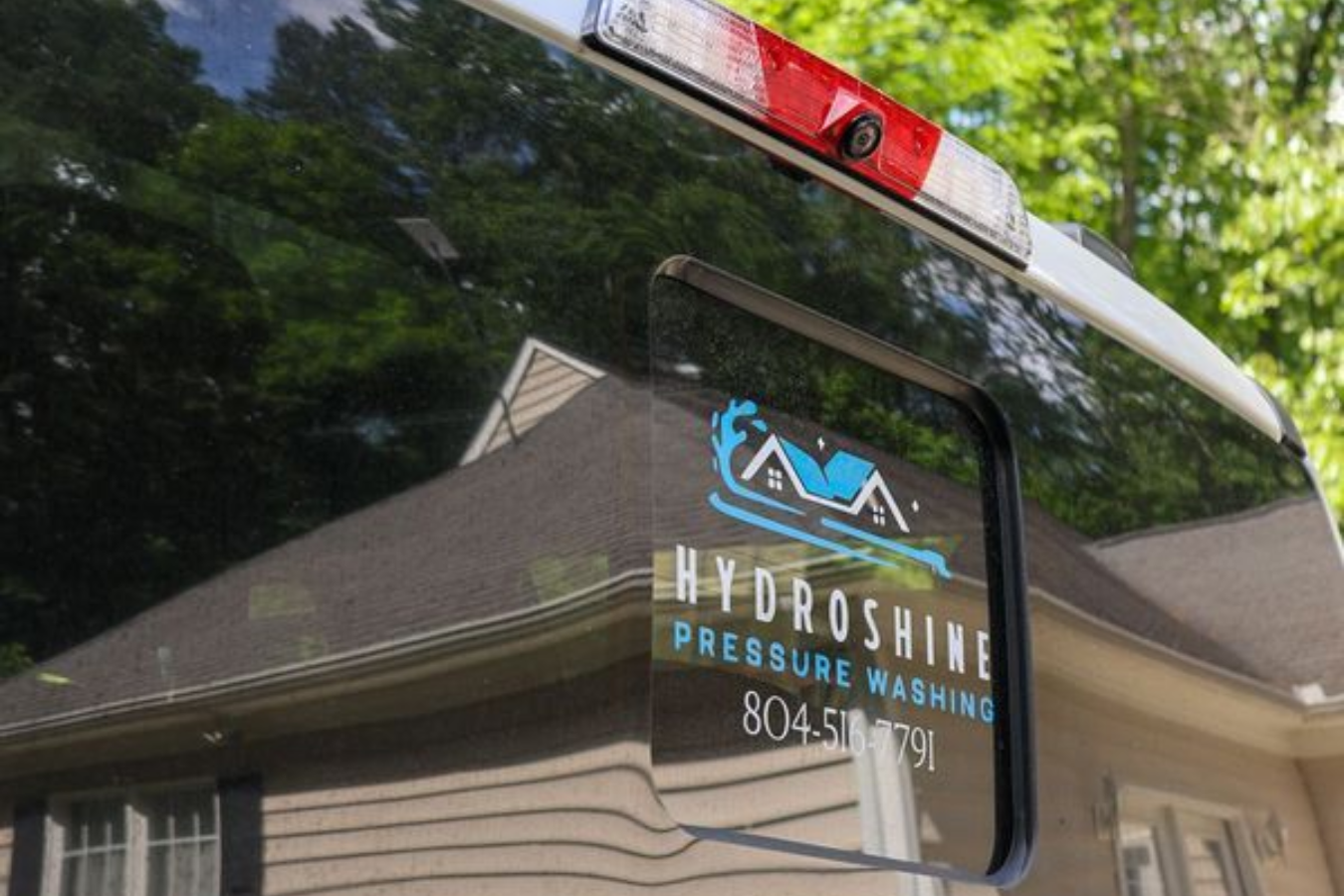 Hydroshine Pressure Washing truck logo on a vehicle window, with trees reflected in the glass.