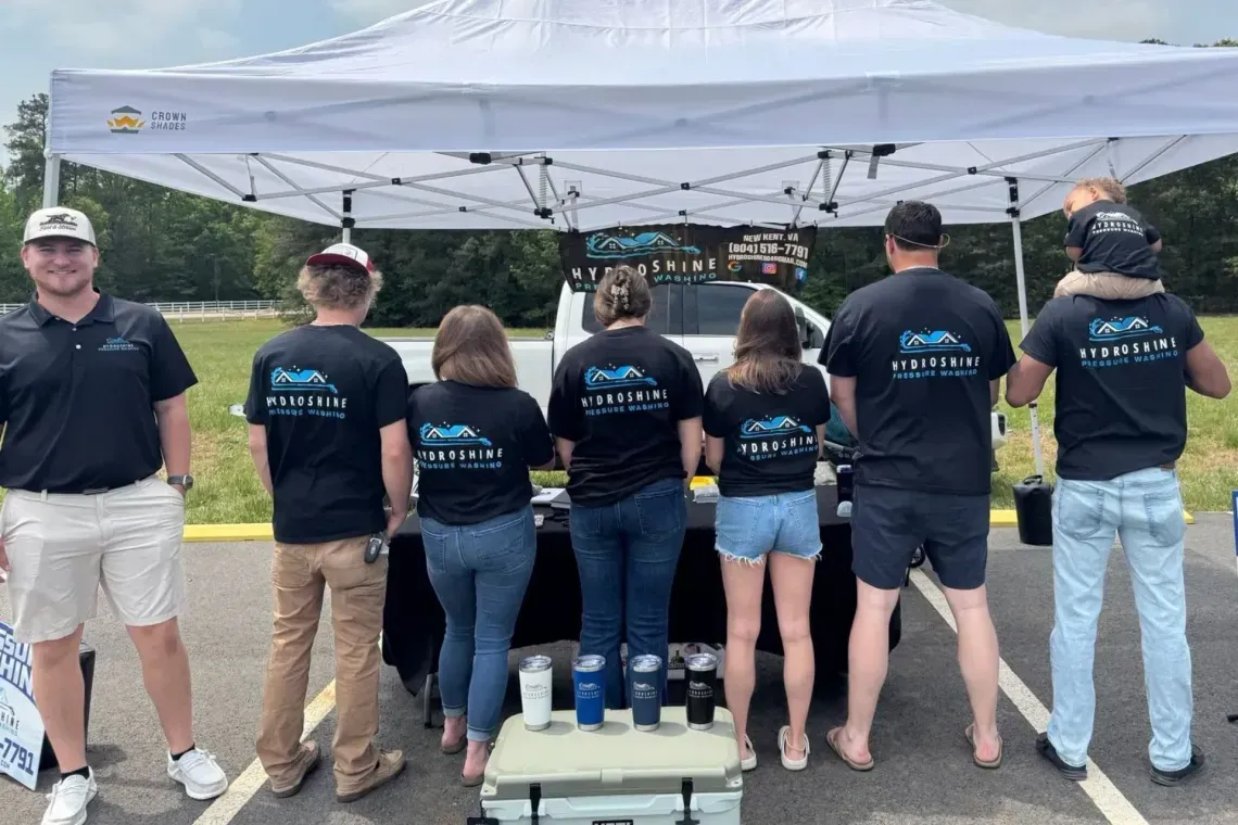 People in matching black shirts stand under a white canopy at an outdoor event.