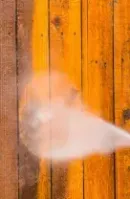 Pressure washing a wooden fence, spraying water on orange and brown vertical planks