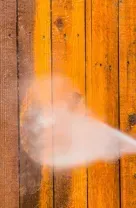 Pressure washing a wooden fence, spraying water on orange and brown vertical planks