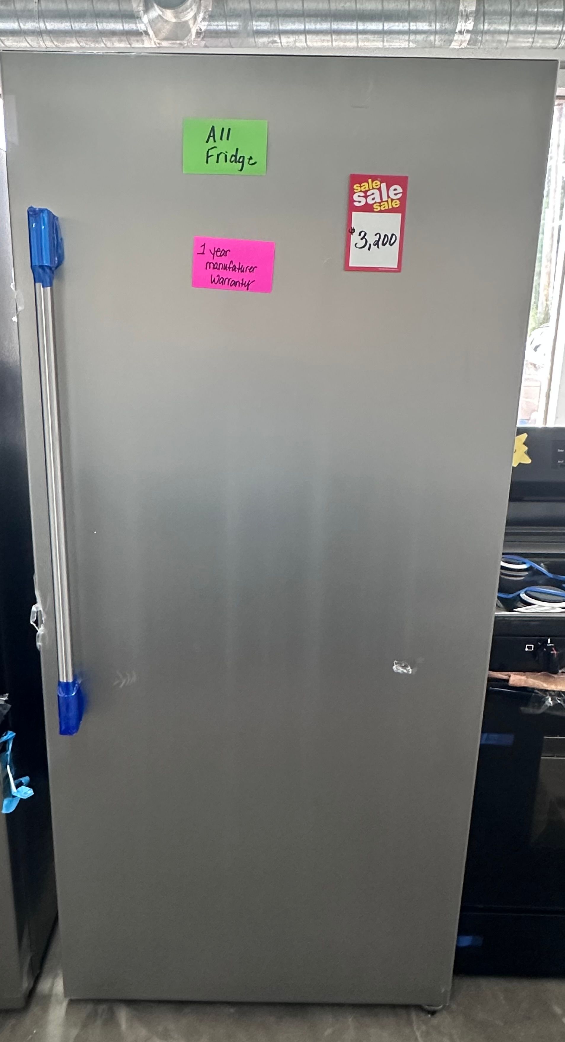 Gray metal refrigerator with colorful labels on the door and blue handles, standing in a kitchen area
