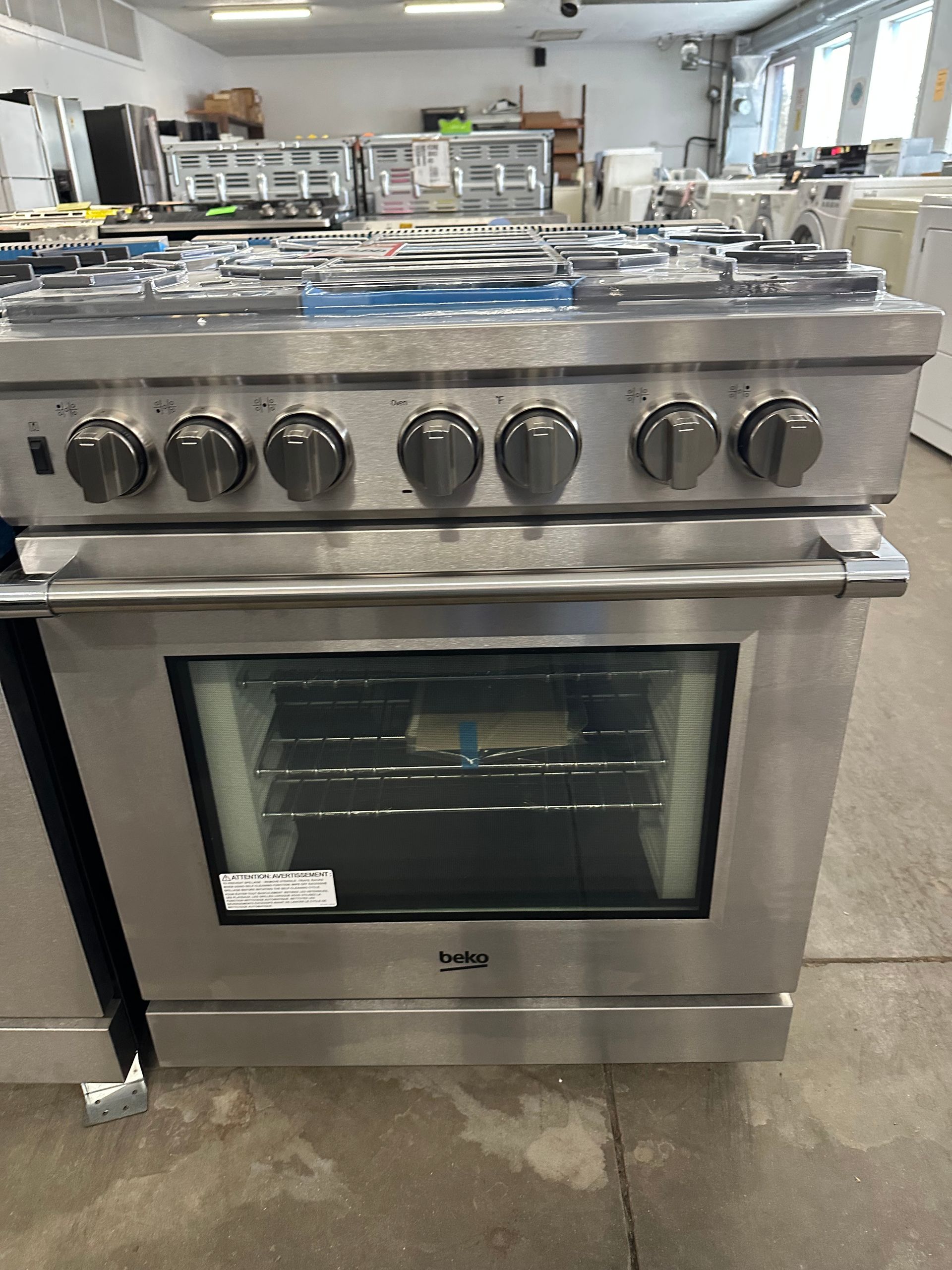 Stainless steel gas range with six burners and an oven, in a showroom.