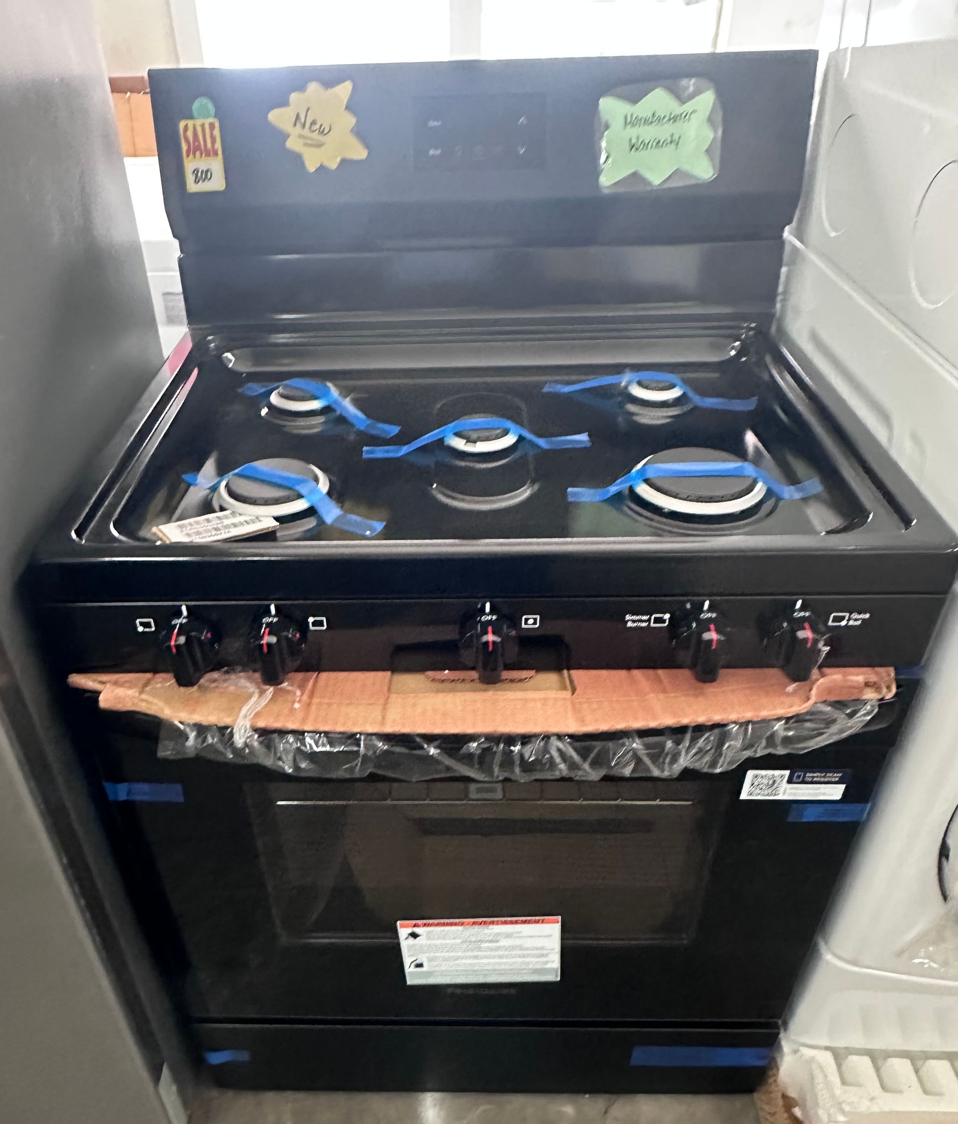 Black gas stove with four burners and oven, in a kitchen-like appliance display.
